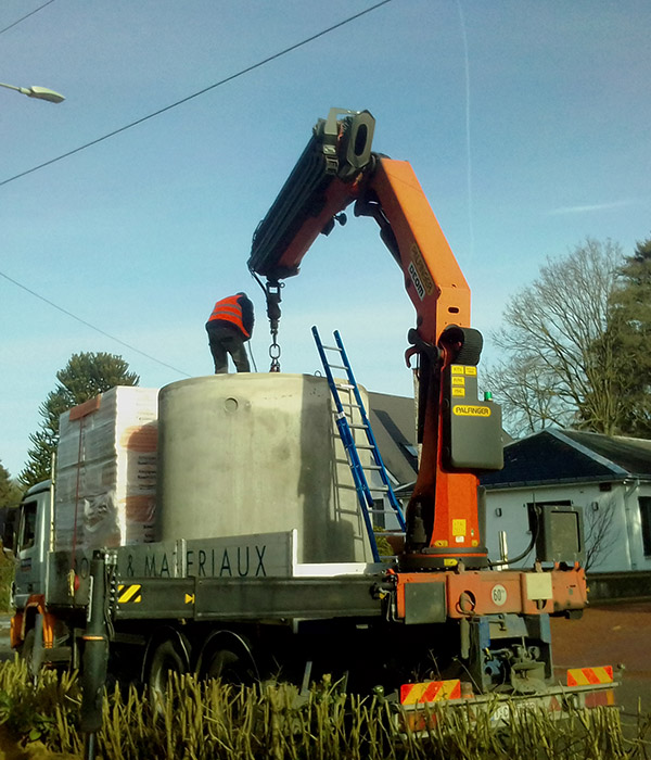 Opérateur installant une cuve en béton à l’aide d’une grue hydraulique montée sur un camion lors de travaux d’aménagement.